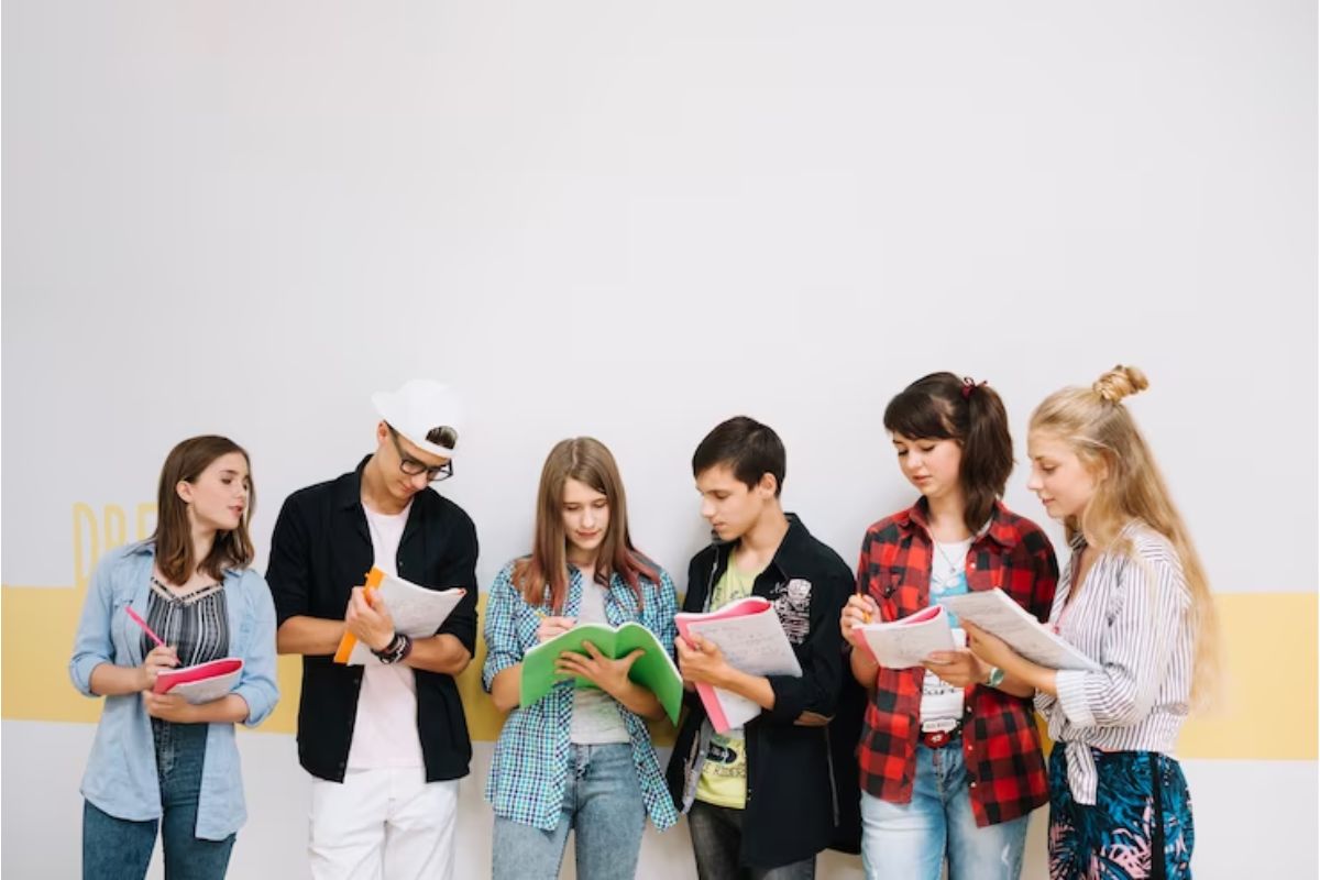 Um grupo de estudantes, um ao lado do outro em frente a um muro da escola 