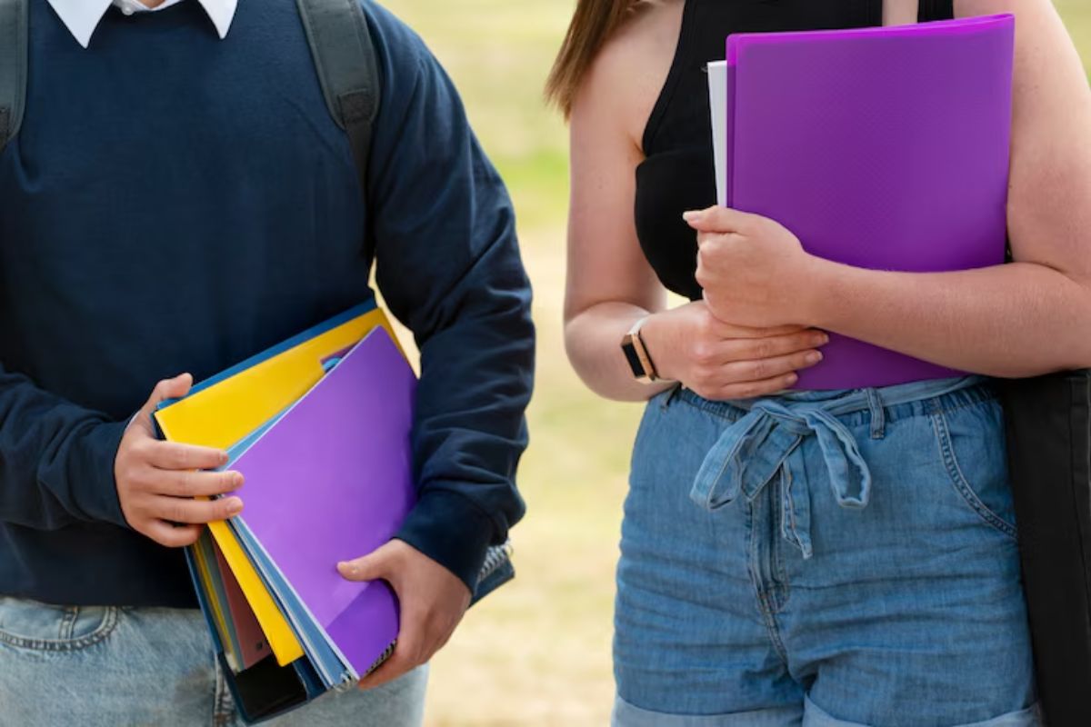 Duas estudantes vistas no jardim da faculdade com seus materiais no colo