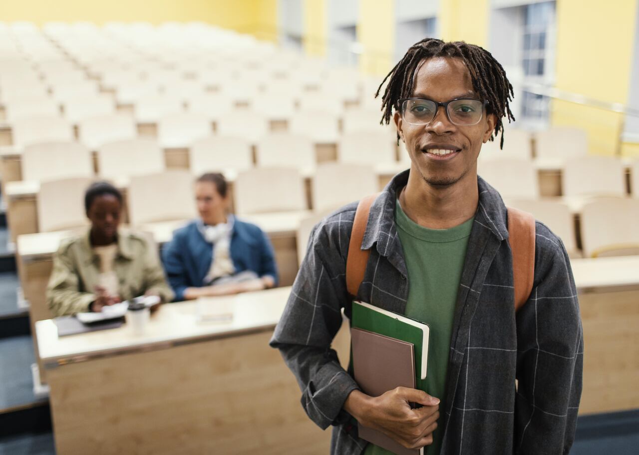 Jovem universitário posa na sala de aula sorridente com colegas ao fundo 