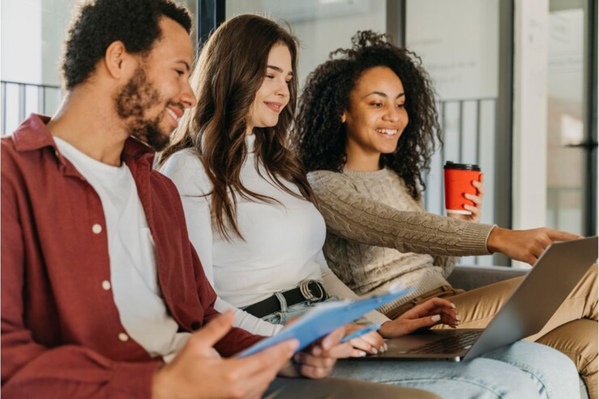 Três estudantes em casa. Uma aluna está com o notebook no colo enquanto outra aponta para a tela desvendando as notas de corte do SISU 2025