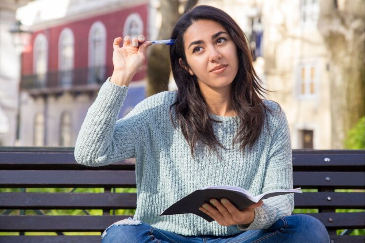 Uma menina sentada no banco com o caderno na mão pensa "Não fui aprovado no SISU 2025". ela leva um lápis à cabeça 