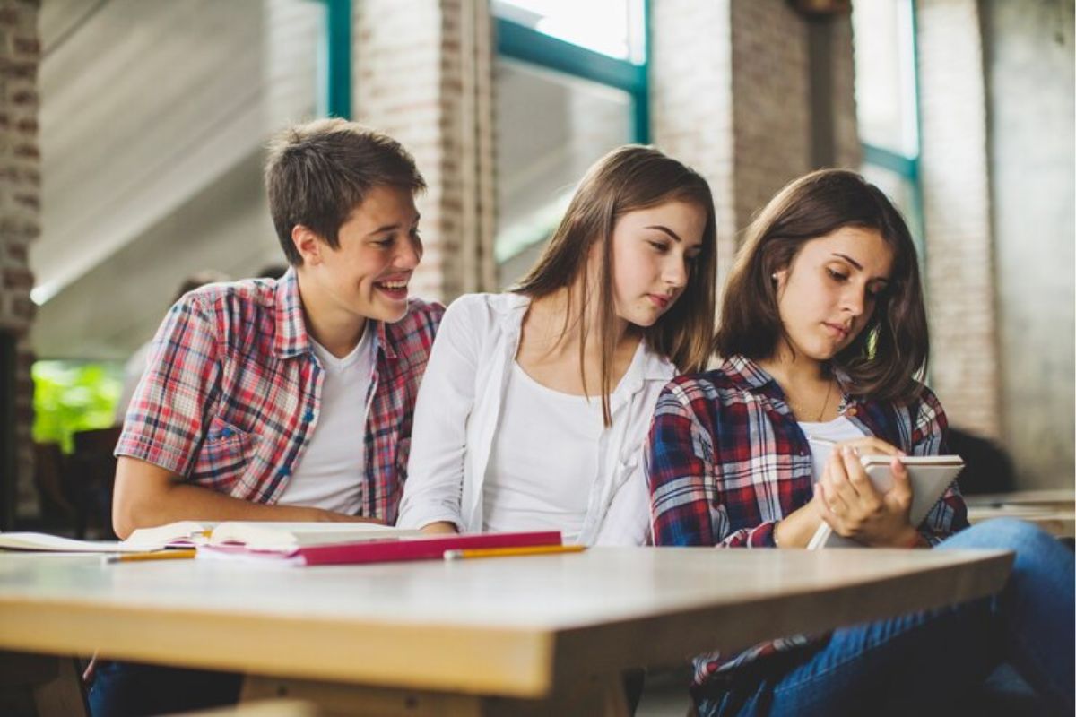 Três estudantes sentados dentro da sala de aula estudam juntas 