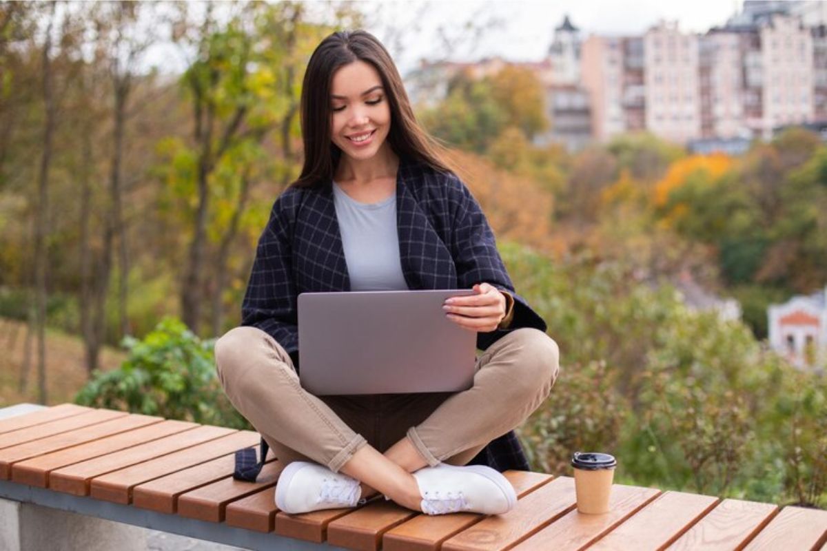 Uma estudante ao ar livre sentada com o notebook no colo