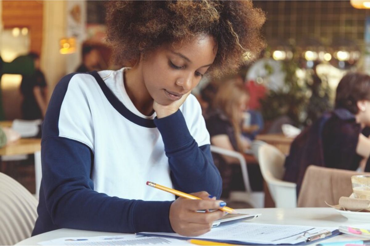 Uma estudante no refeitório escrevendo em seu caderno