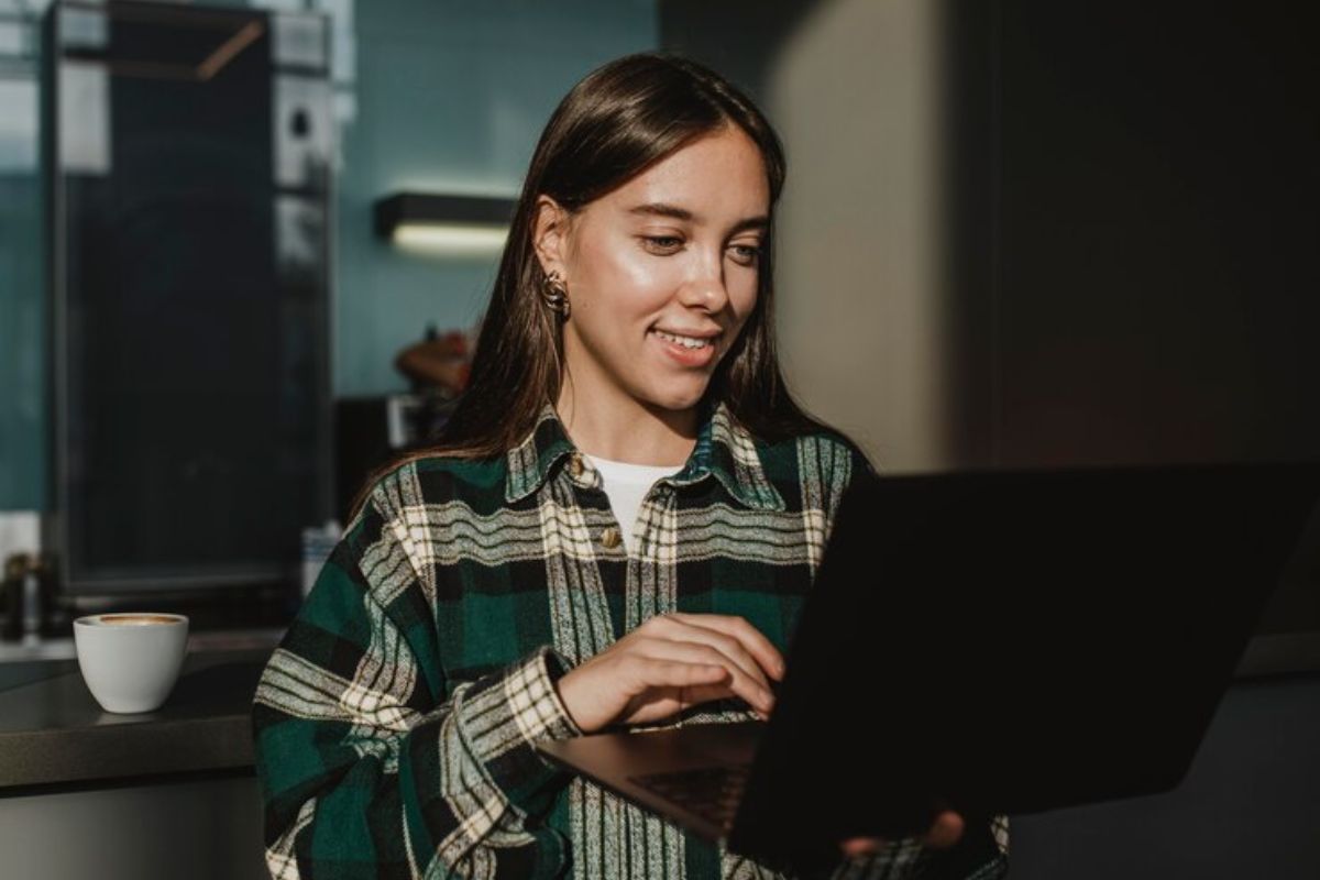 Uma mulher com seu notebook na mão procura quais são os cursos com notas de corte mais baixas de toda história do SISU