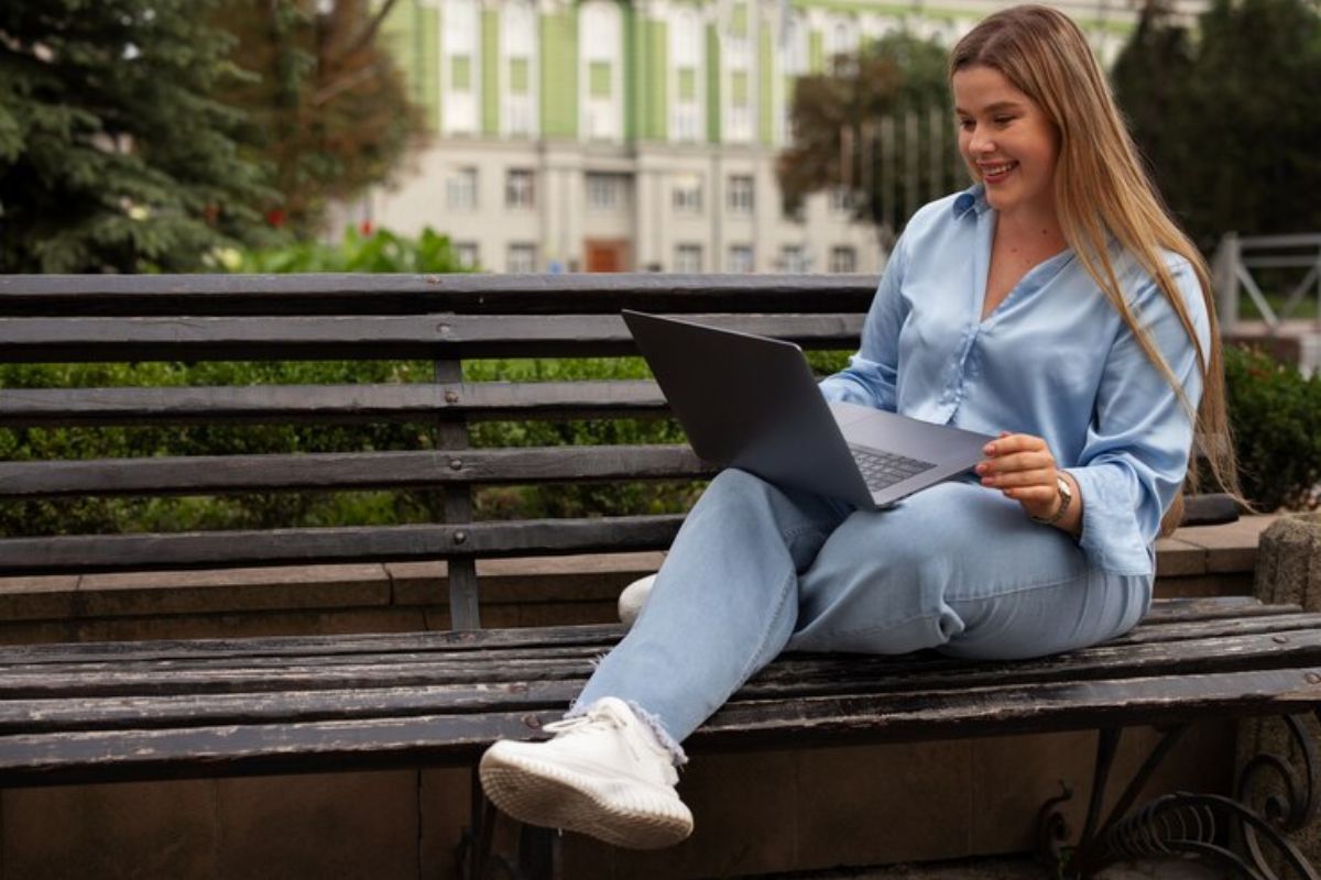 Uma estudante no banco da praça com o notebook no colo confere o Resultado do SISU 2025