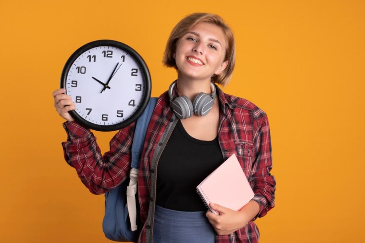 Uma estudante segura um relógio com uma mão e na outra um caderno